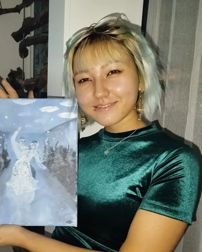 Jenny Wolff hält ein von ihr gemaltes Szenenbild eines tanzenden Brautpaars in die Kamera